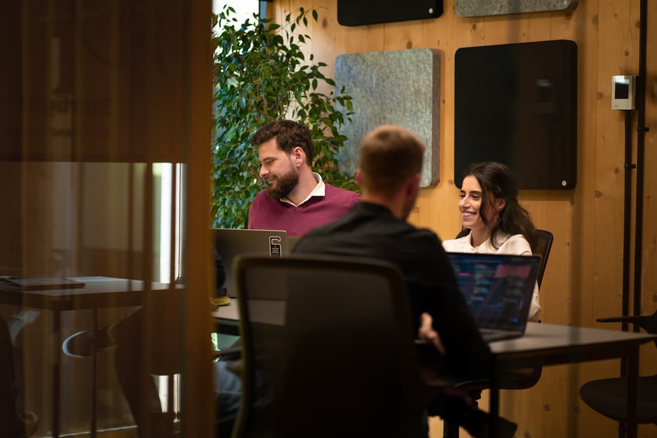 Colleagues collaborating with laptops in a glass-walled coworking space